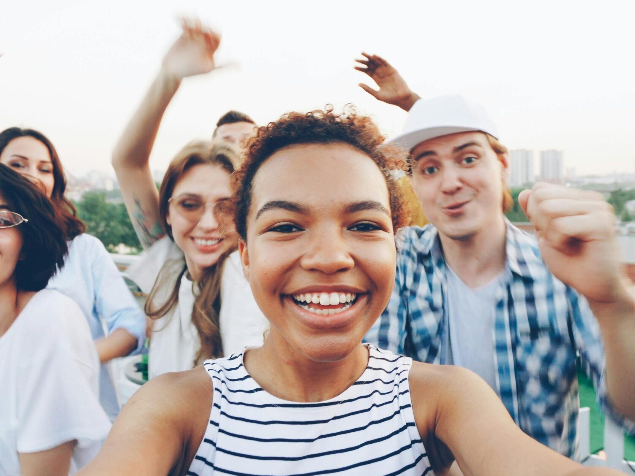 Group of friends enjoying a lively rooftop party together, smiling and waving.