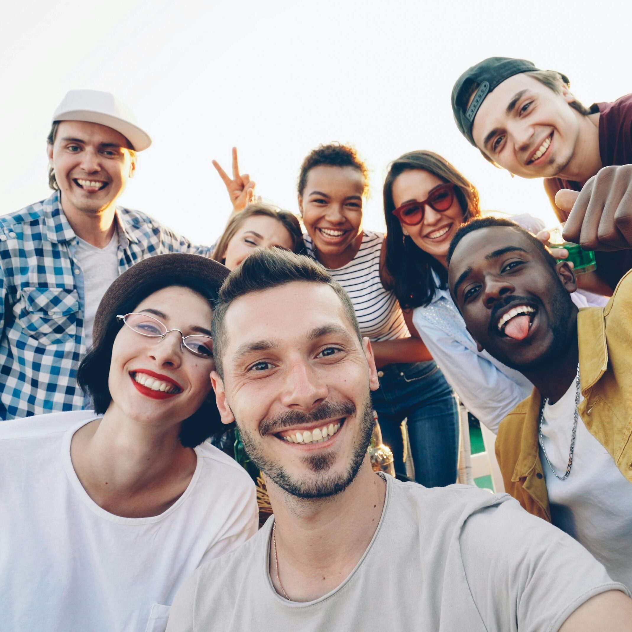 A diverse group of friends smiles while taking a selfie outdoors during the day.